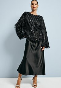 Černý flitrový top s třásněmi, kombinovaný s elegantní černou saténovou sukní a sandály s ozdobnými pásky.