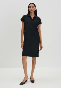 Robe noire à manches courtes avec col, longueur genou, en tissu lisse. Présente une coupe droite et un détail de ourlet discret.