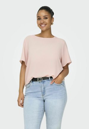 Ljusrosa kortärmad blus med avslappnad passform, rundad halsringning och textilstruktur. Kombineras med ljusblå denimjeans och ett svart bälte.
