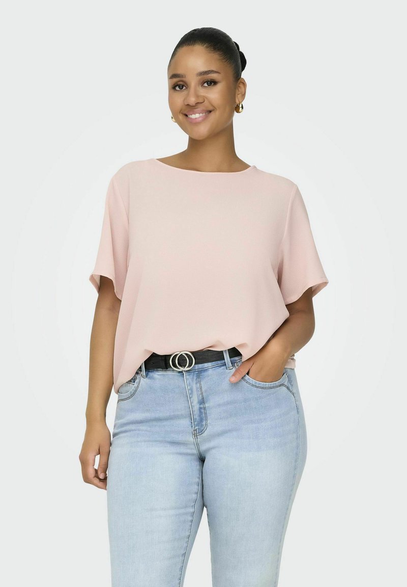 Jasnoróżowa bluzka z krótkim rękawem o luźnym kroju, z zaokrąglonym dekoltem i teksturowanym materiałem. W połączeniu z jasnoniebieskimi dżinsami i czarnym paskiem.