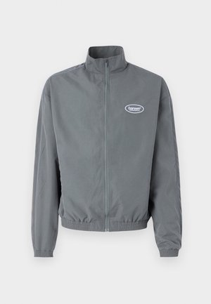 Sivina zip-up jakna iz gladke tkanine, z visokom ovratnikom, elastičnim pasom in majhnim logotipom na levem prsnem delu.