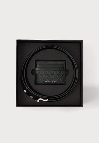 Ceinture en cuir noir enroulée autour d'un porte-cartes Michael Kors en cuir noir à l'intérieur d'une boîte cadeau noire.