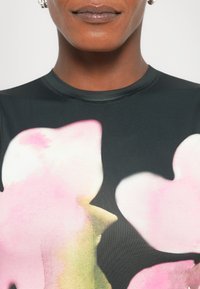 Svart stofftopp med store rosa blomstermønster i akvarell; nærbilde av halslinje og skulder med glatt tekstur og tettsittende design.