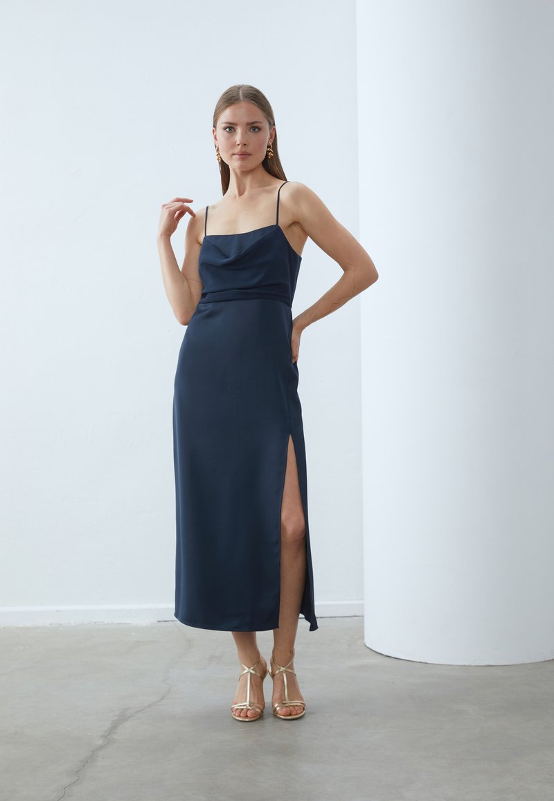 Námořnické saténové šaty s lodičkovým výstřihem, tenkými ramínky, bočním rozparkem a přiléhavým střihem. Doplněné sandály na tenkých podpatcích v metalickém provedení.