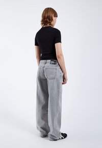 Zwarte top met korte mouwen, gecombineerd met lichtgrijze high-waisted broek met wijde benen. De broek heeft een klassiek vijf-pocket ontwerp en een logo-patche op de achterkant.