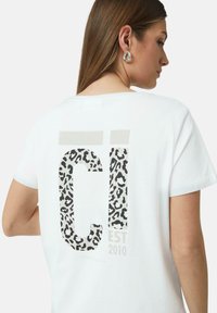 Weißes Baumwoll-T-Shirt mit einem Leopardenmuster-Design in den Buchstaben "C" und "I" auf dem Rücken. Enthält den Text "EST 2010" unter dem grafischen Element.