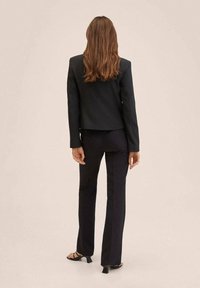 Sort skræddersyet blazer med en struktureret pasform, lukning med én knap og matchende sorte bukser. Båret med åbne hæle. Simpelt design.