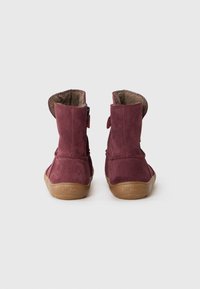 Bottines chelsea en suede bordeaux avec une doublure douce, des bouts ronds et des semelles en caoutchouc marron flexibles, dotées de fermetures Velcro sur le côté.