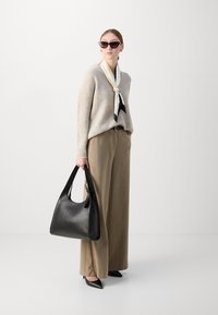 Black leather handbag with a hobo shape, paired with a beige knit sweater, striped wide-leg trousers, and pointed black heels. Accessories include a white and black patterned scarf and cat-eye sunglasses.