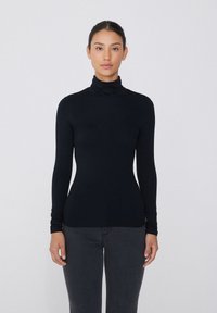 Un haut à col roulé noir en tissu extensible, avec des manches longues et une coupe ajustée qui épouse les formes du corps, associé à un jean sombre.