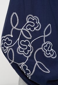 Ύφασμα ναυτικό μπλε με λευκά κεντητά ανθικά μοτίβα, που παρουσιάζουν ένα σχέδιο κληματαριάς με βρόχους και πέταλα. Λείο υλικό, απαλό πέσιμο.