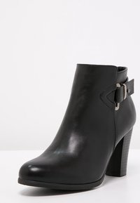 Black leather ankle boot with a pointed toe, high block heel, and side buckle detailing. Smooth texture, minimalist design.