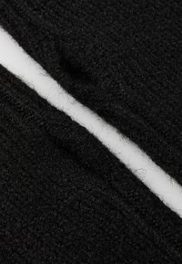Primo piano di un tessuto nero a maglia con una cucitura visibile che corre in diagonale su uno sfondo bianco.