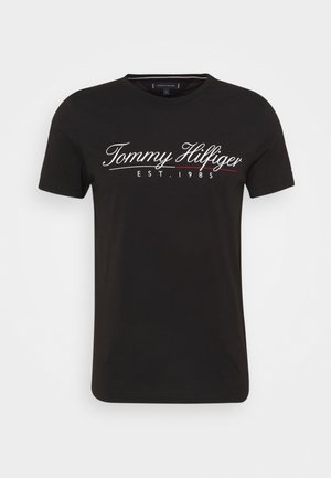 Czarna koszulka z krótkim rękawem z białym kursywnym tekstem "Tommy Hilfiger" i "EST. 1985" na piersi.