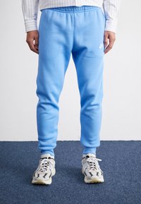 Svetlomodré tepláky s elastickým pásom, hladkou textúrou, zúženými nohavicami a malým bielym logom Nike na ľavej strane.