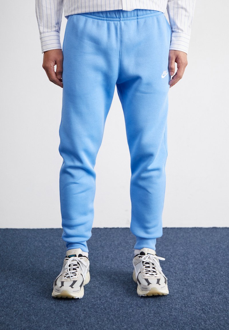 Svetlomodré tepláky s elastickým pásom, hladkou textúrou, zúženými nohavicami a malým bielym logom Nike na ľavej strane.