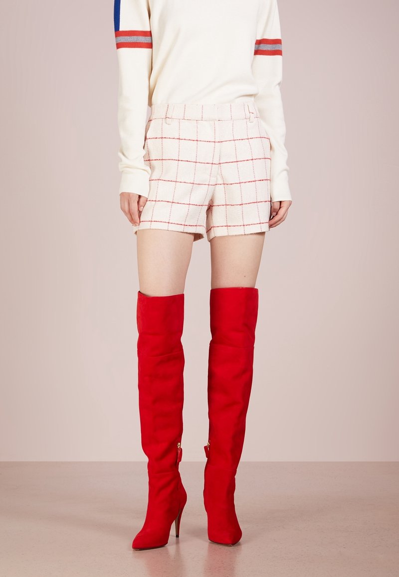 Pull en mélange de laine avec des rayures rouges et bleues, associé à un short taille haute en tweed crème avec un motif à carreaux rouges et des bottes rouges jusqu'à la cuisse.