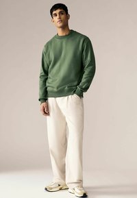 Groene sweatshirt met geribbelde manchetten en zoom, gecombineerd met crèmekleurige, loszittende broek en witte sneakers met gele accenten. Zachte stoftextuur.