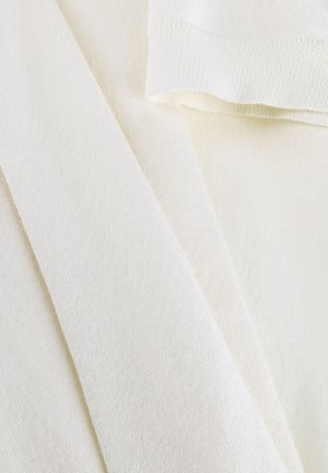 Zacht roomkleurig stof met zichtbare textuur, plooien en randen, die lijkt op breigoed of kledingmateriaal.