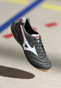 Pantofii de fotbal indoor gri cu accente negre, design triunghiular alb, detalii roșii și un material texturat. Talpa din gumă pentru aderență.