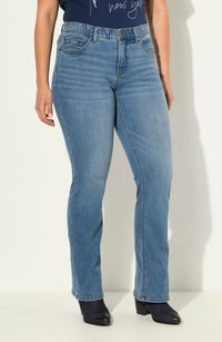 Jeans in denim azzurro chiaro con gamba tapered, vita elasticizzata, tasche anteriori e chiusura con bottone. Indossati con stivali neri con tacco.