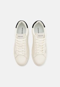 Vita sneakers med en slät läderstruktur, snörning och svarta detaljer på häl och krage; har en sidopanel i mesh.