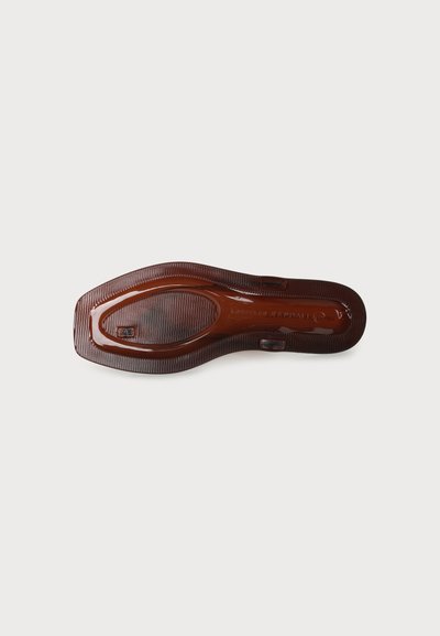 Semelle d'une chaussure en cuir marron avec une semelle antidérapante texturée et le nom de la marque embossé sur un fond clair uni.