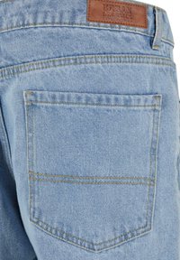 Ljusblå denimjeans med en texturerad yta, med en bakficka och en brun läderetikett sydd vid midjan.