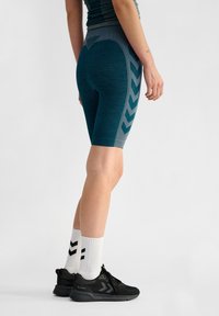 Turkosa cykelshorts med en texturerad yta och en kontrasterande grå zigzag-mönster på sidan. I kombination med svarta löparskor och vita strumpor.