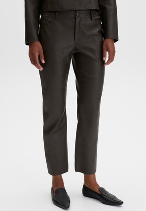 Person wearing dark brown cropped leather pants with matching jacket and black pointed loafers, standing against plain background.