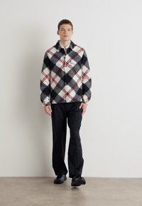 Plaid flannel shirt in black, white, and burgundy, with a button-up design and long sleeves, paired with black trousers and shoes.