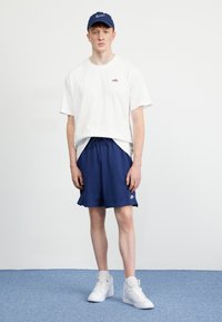 T-shirt bianca in cotone, pantaloni corti navy con cordino, logo Nike bianco. Sneakers alte bianche. Design semplice, abbigliamento casual atletico.