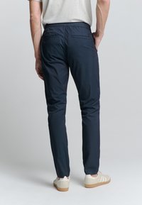 Marineblauwe, lichtgewicht broek met een rechte pijp, elastische tailleband en twee achterzakken; gecombineerd met lichtgekleurde sneakers.