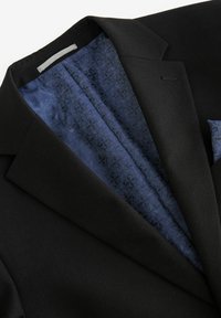 Schwarzer Blazer aus strukturiertem Stoff, mit Reverskragen und einer blauen gemusterten Fütterung, die im offenen Vorderteil sichtbar ist. Enthält ein Einstecktuch.