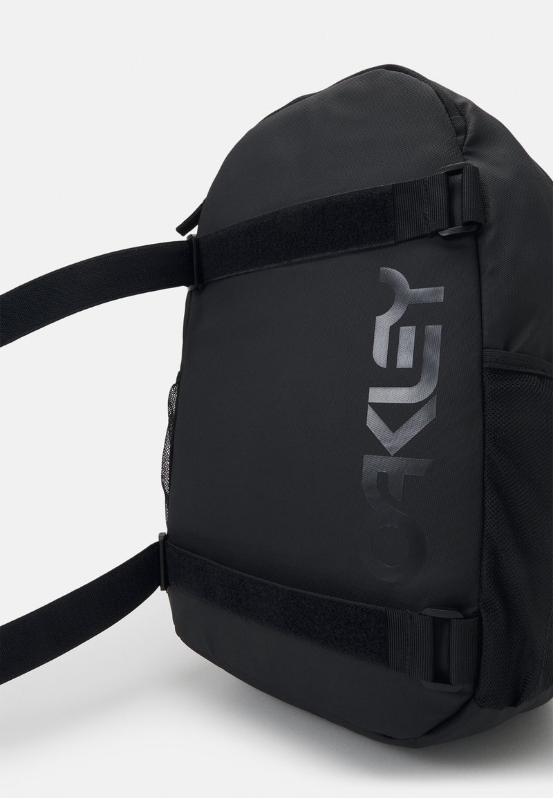 Black backpack made from durable fabric; features adjustable straps, a mesh side pocket, and a prominent glossy logo. Compact and structured design.