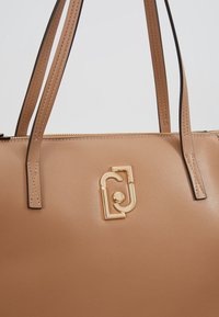 Brązowa torebka skórzana z podwójnymi paskami, z akcentem w złotym kolorze i teksturowanym wykończeniem, zamykana na zamek błyskawiczny u góry, minimalistyczny design.