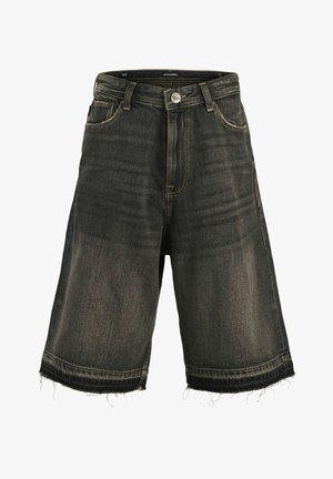 Junge steht, trägt ein kurzärmeliges Hemd mit Muster über einem weißen T-Shirt, dunkle Jeansshorts, hohe weiße Socken und braune Schnürschuhe.