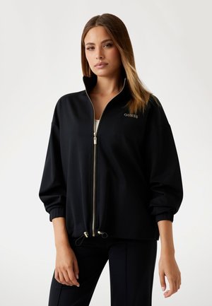 Zwarte zip-up sweatshirt met een hoge kraag, elastische manchetten en gouden ritsen. Bevat het "GUESS" logo in een subtiele lettertype op de borst.