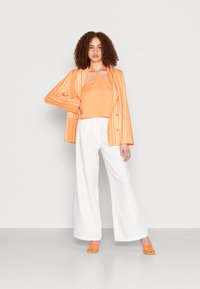 Blazer listrado laranja sobre uma blusa regata laranja, combinado com calças largas brancas e saltos laranja. Tecido suave com um corte descontraído.