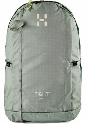Lichtgrijze compacte rugzak met verticale riem, zijgespen en "TIGHT LIGHT"-branding aan de voorkant.