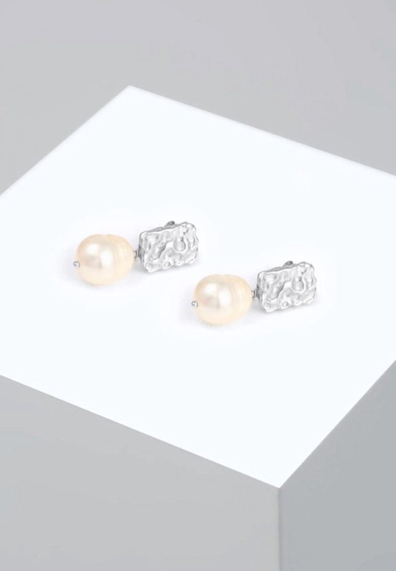 Paquet de boucles d'oreilles clips en argent avec des carrés texturés irréguliers et de grosses perles couleur crème sur un socle blanc.