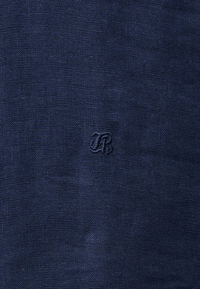 Σκούρο μπλε ύφασμα με ένα μικρό, διακριτικό κεντητό μονόγραμμα «JR» στο κέντρο της επιφάνειας.