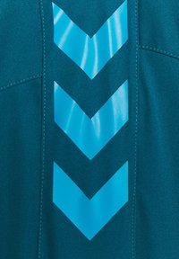 Teal stof med tre store, blanke blå chevronmønstre. Teksturen er glat med kontrasterende syninger langs sømmene.