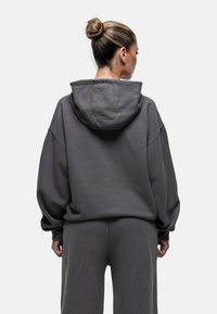 Haut à capuche surdimensionné gris avec cordon de serrage, épaules tombantes et manches longues, fabriqué à partir d'un tissu doux et texturé, associé à un pantalon assorti.