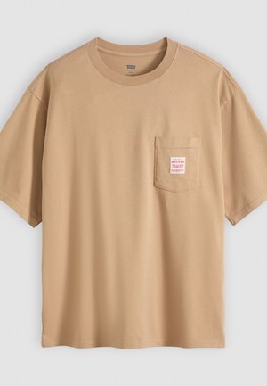 Beige, lockere Kurzarm-T-Shirt mit Rundhalsausschnitt und einer Brusttasche, die ein kleines rot-weißes rechteckiges Etikett zeigt.