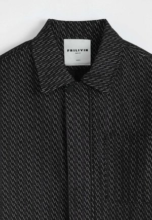 Veste noire texturée avec des surpiqûres blanches en diagonale, col, fermeture à boutons-pression, et une étiquette blanche indiquant "FRILIVIN PARIS.FR SIZE S".