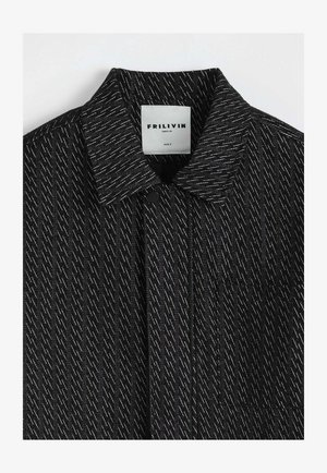 Veste noire texturée avec des surpiqûres blanches en diagonale, col, fermeture à boutons-pression, et une étiquette blanche indiquant "FRILIVIN PARIS.FR SIZE S".