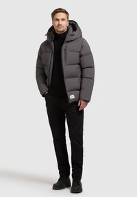 Grijze gewatteerde jas met een capuchon, voorzien van een zip pocket, gecombineerd met zwarte broeken en schoenen. Glad textuur met een gelijkmatige kleurfinish.