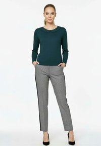 Dark green long-sleeve top with a round collar, paired with gray checkered trousers featuring black side stripes and worn with black heels.