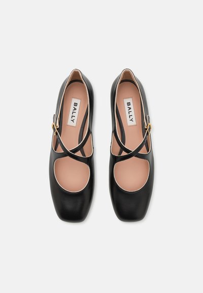 Zapatos de cuero negro con detalles recortados y diseño de tiras cruzadas. Puntera redondeada, estilo deslizante y sutiles acentos en dorado.